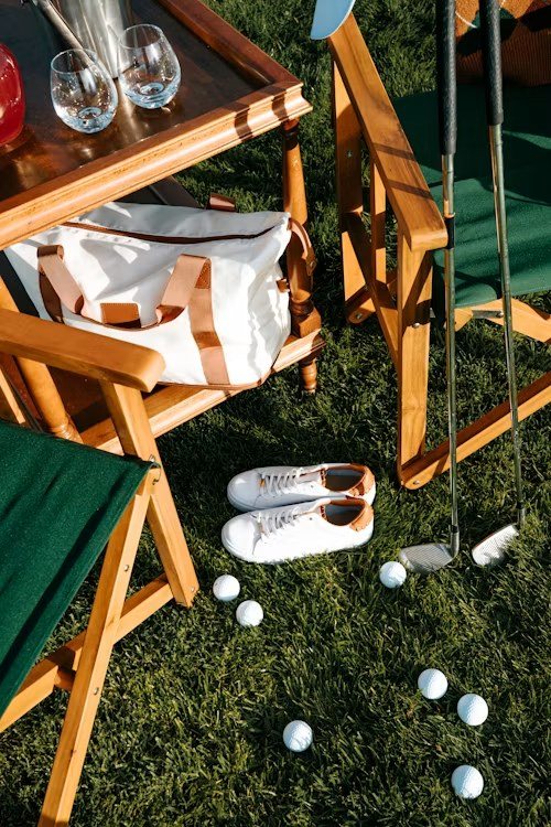Folding wood-and-canvas chairs, white shoes and golf balls on the grass beside a picnic table